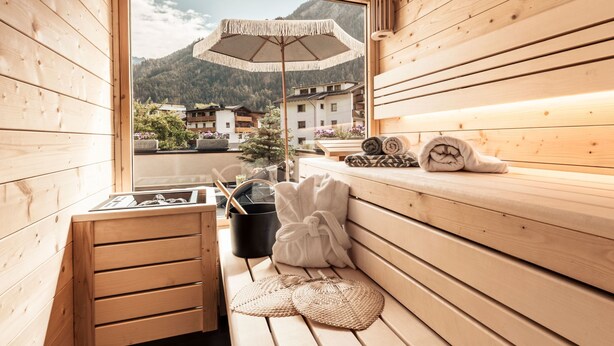 A wooden sauna with a view of mountains, a bench, towels, and a woven mat. - Apart  Bieles NEU by Interhome (Kauns)