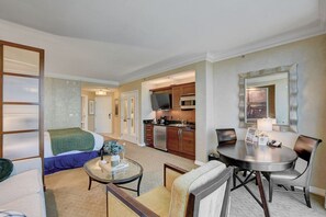 A hotel room with a bed, a glass coffee table, a dining table with chairs, a kitchen area with cabinets and appliances, and a large mirror on the wall. - Deluxe Balcony Strip View MGM Signature (Las Vegas)