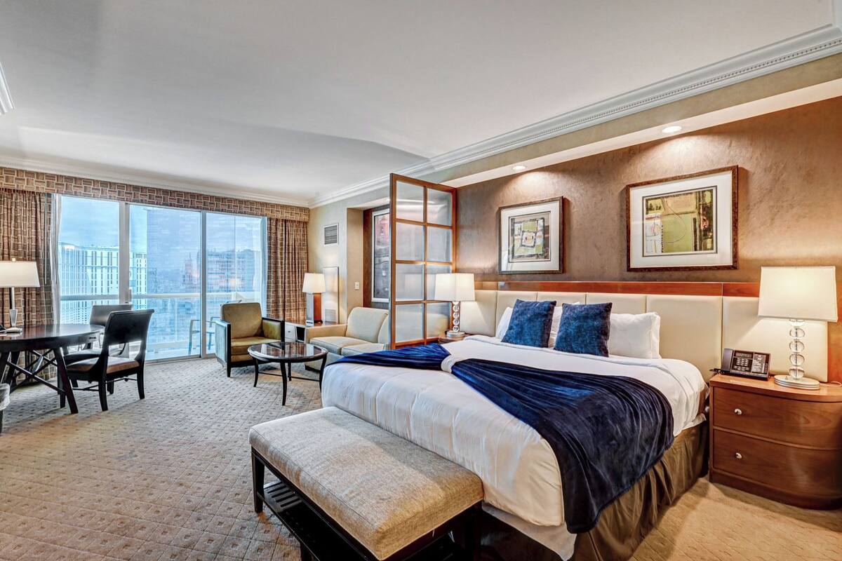 Une chambre d’hôtel avec un grand lit, un bureau, deux chaises, une petite table et une vue sur la ville.