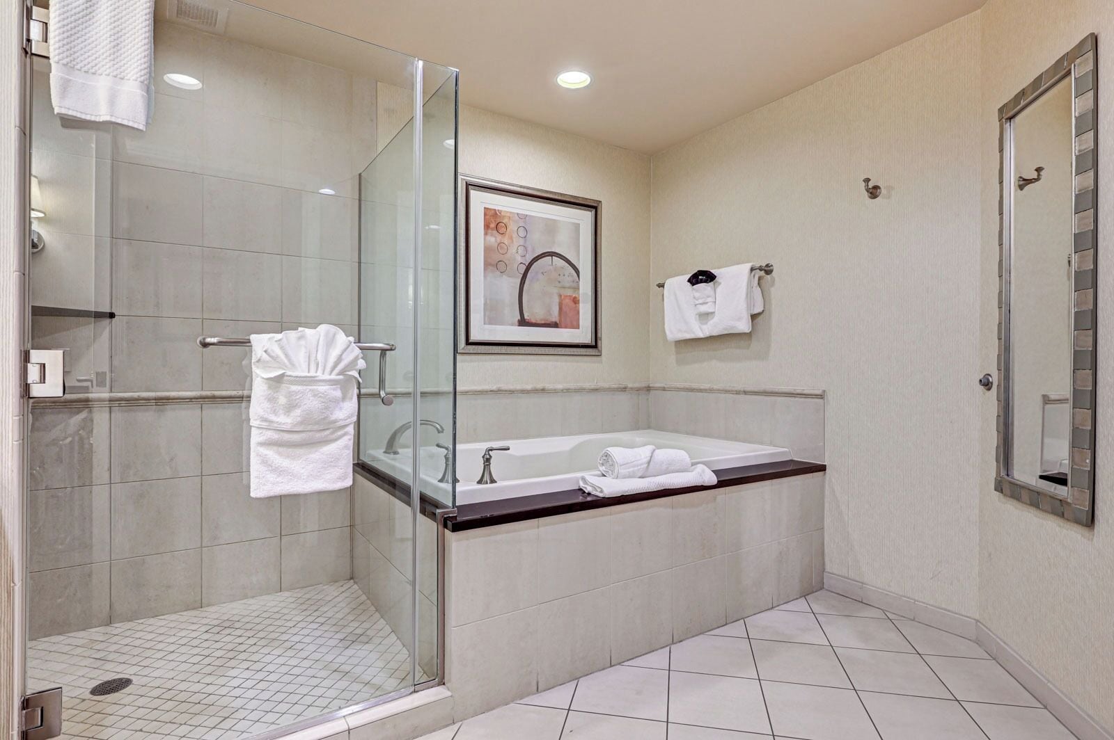 Een moderne badkamer met een douche met glazen wand, een groot bad en een kunstwerk in een lijst aan de muur.
