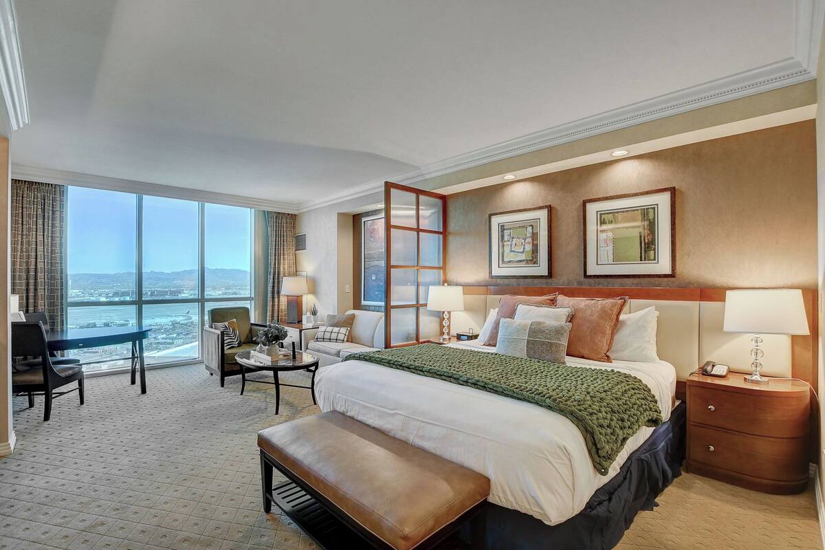 Une chambre d’hôtel avec un grand lit, un bureau, une chaise, une vue sur la ville et un balcon.
