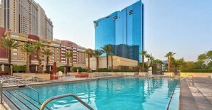 A hotel with a swimming pool, palm trees, and modern buildings in the background. - Deluxe Balcony Strip View MGM Signature (Las Vegas)