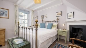 Una camera da letto con un letto, un comodino, una cassettiera, un caminetto e una finestra con tende.