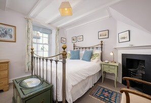 A bedroom with a bed, a nightstand, a dresser, a fireplace, and a window with curtains. - Hardys is a charming traditional fisherman's cottage nestled in the heart of Padstow (Padstow)