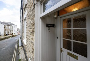 A street view with a building labeled 'Hardys 31' featuring a white door with a brass handle and a window with a decorative pattern. - Hardys is a charming traditional fisherman's cottage nestled in the heart of Padstow (Padstow)