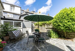 A patio with a table and chairs, a green umbrella, and a stone floor. - Hardys is a charming traditional fisherman's cottage nestled in the heart of Padstow (Padstow)