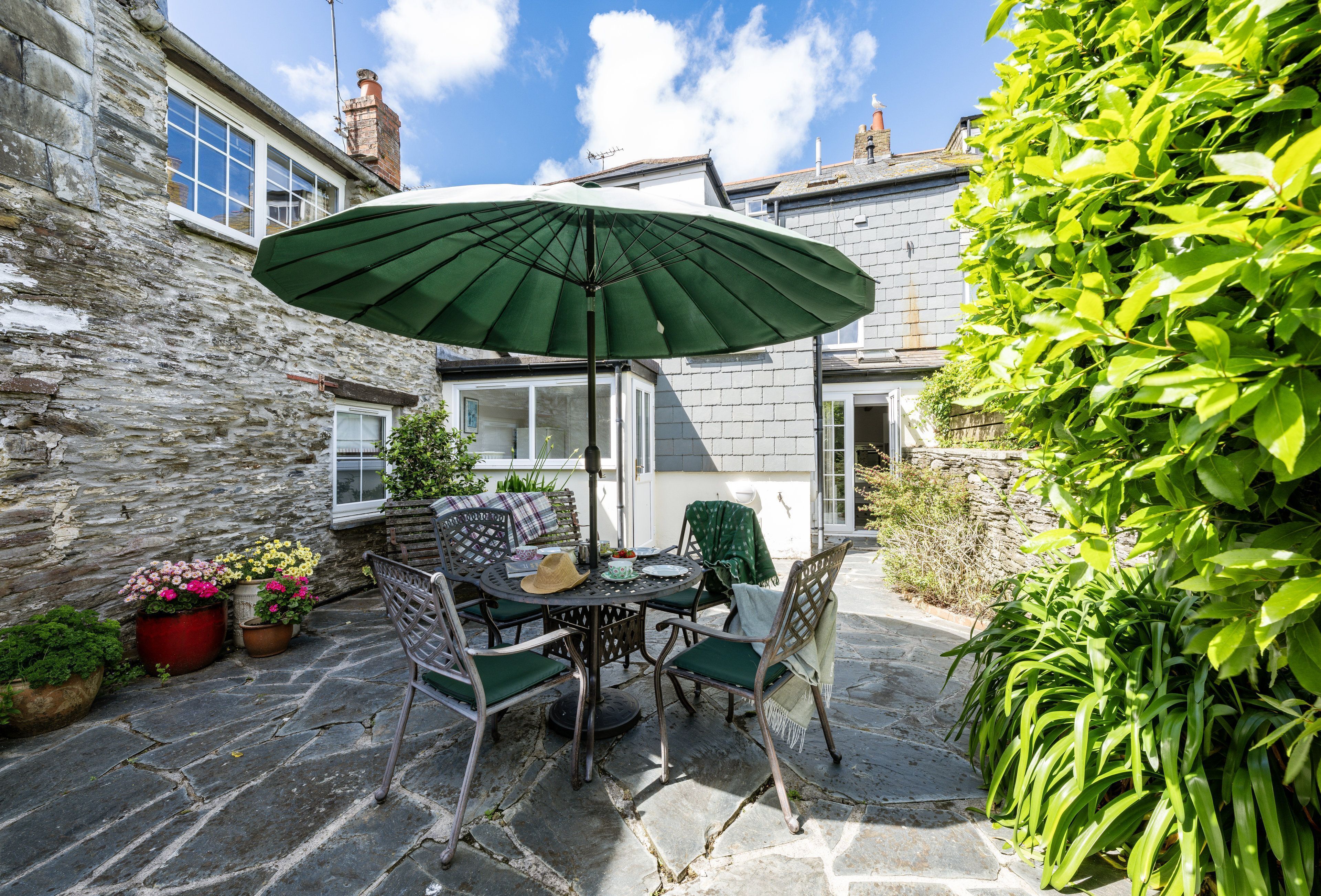 A stone patio with a table and chairs, an umbrella, and potted plants.