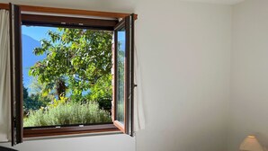 Ett hotellrum med ett stort fönster, en säng, ett nattduksbord med en lampa och en stol.