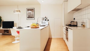 Une cuisine moderne dotée d’un îlot central, d’un coin repas avec une table et des chaises blanches, et d’un téléviseur à écran plat.
