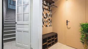 Un pasillo con una puerta blanca, una escalera, un papel tapiz decorado, un banco y una planta en maceta.