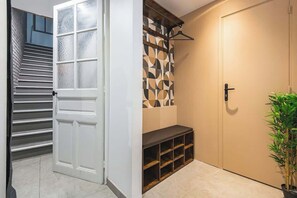A hallway with a white door, a staircase, a patterned wall, a bench, and a potted plant. - MM Suites City House Cathedrale (Reims)