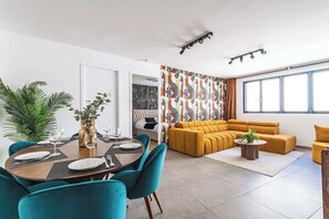 A modern living space with a dining area, a sofa set, and a large window providing natural light. - MM Suites City House Cathedrale (Reims)