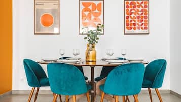 Un comedor con una mesa preparada para cuatro personas, sillas color turquesa y cuadros en la pared.