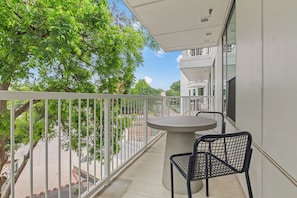 A balcony with a round table and two chairs, overlooking a street with trees and buildings. - 1BR Suite w/ Private Balcony | Pool + Terrace + Restaurant | The Code (Austin)