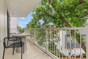 Un balcon avec une table et des chaises, une balustrade blanche et une vue sur les maisons et les arbres des environs.