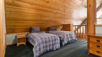 A wooden-paneled room with two beds, a small dresser, and a window with a view.