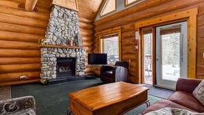 A log cabin interior with a stone fireplace, a television, and a cozy seating area.