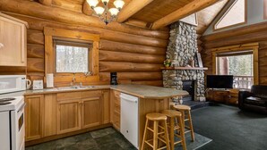 A log cabin interior with a kitchen, bar area, and stone fireplace.