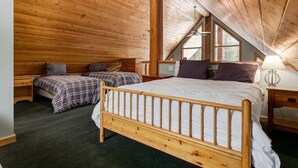 A cozy attic bedroom with wooden walls, a large bed, two smaller beds, and a window providing natural light.