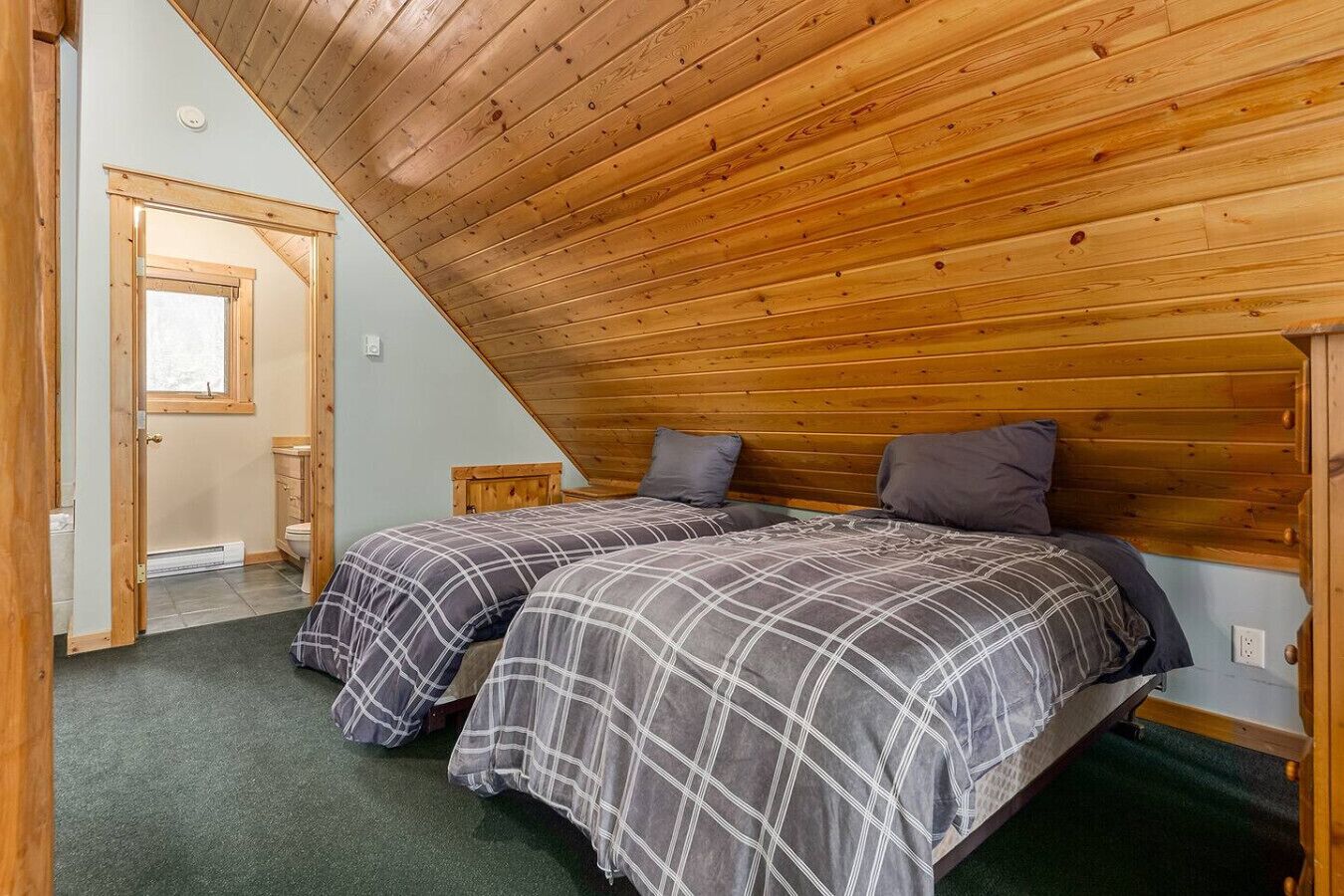 A bedroom with two beds, wooden ceiling, and a door leading to a bathroom.