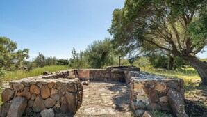 Un'antica struttura in pietra con un percorso centrale e mura di pietra, circondata da alberi ed erba.