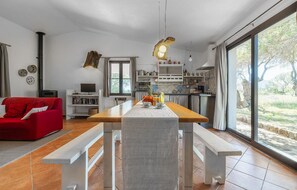 A modern living room with a red sofa, a wooden dining table with benches, a kitchen with a large window, and a fireplace. - Stunning home in Orosei with WiFi (Orosei)
