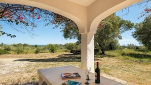 Un'area salotto esterna riparata, con un tavolo, libri, una bottiglia di vino e bicchieri.