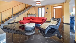 A modern living room with a red sectional sofa, a unique black and blue chair, a round coffee table, and a staircase with a glass railing. - 3 bedroom gorgeous home in Torre Le Nocelle (Torre Le Nocelle)