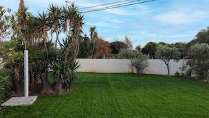A well-maintained grassy backyard with a white wall, a utility pole, and various trees. - Beautiful home in Ispica with WiFi (Ispica)