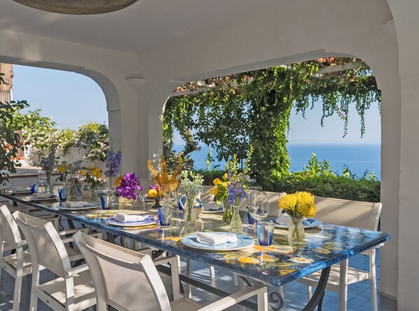 An outdoor dining area with a table set for two, overlooking a scenic view of the sea.
