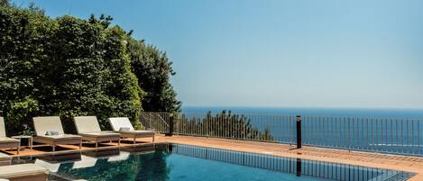 Un espace piscine avec des chaises longues et vue sur la mer.