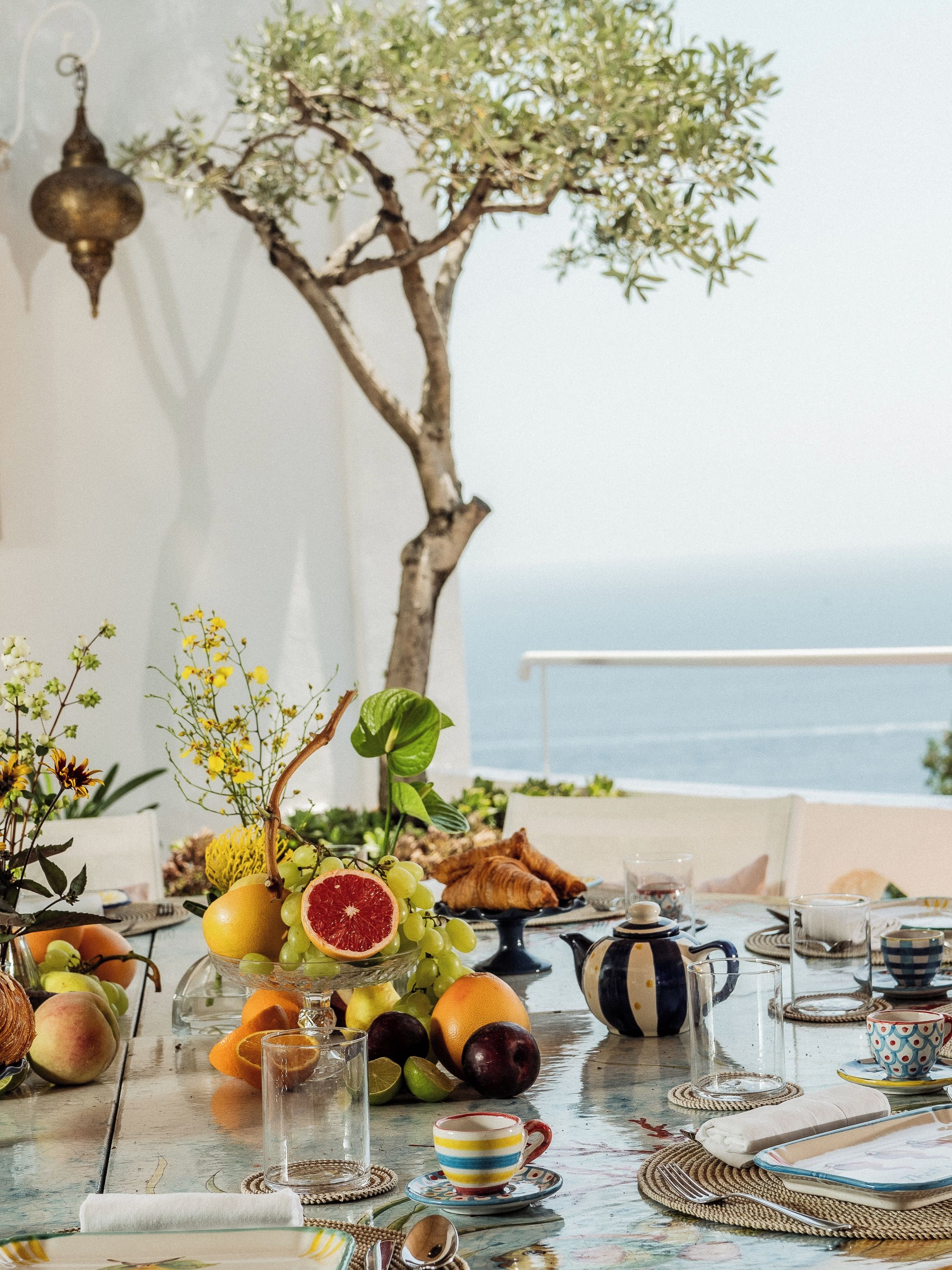 Une table dressée avec des fruits, des pâtisseries et une vue sur la mer.