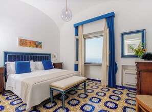 A hotel room with a bed, a bench, a window with curtains, a painting, and a mirror.