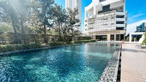A swimming pool with clear water, surrounded by trees and modern buildings. - two-bedroom Beachfront at Veranda Residence (Sattahip)