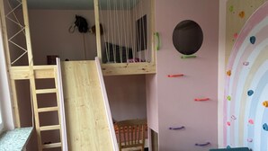 Une salle de jeux pour enfants avec un toboggan en bois, un mur d’escalade et un lit superposé.