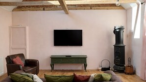 Un salon chaleureux avec un plafond en bois, un téléviseur à écran plat, un banc vert et un poêle noir.