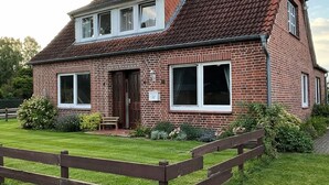 Une maison à deux étages, construite en briques, avec un toit en pente, un porche à l’avant et une clôture en bois.