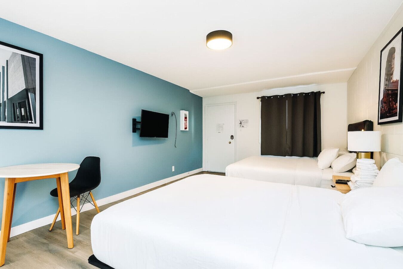 A hotel room with two beds, a desk, a chair, a TV, and a window with curtains.