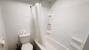 Une petite salle de bain blanche, avec des toilettes, un rideau de douche et une baignoire.