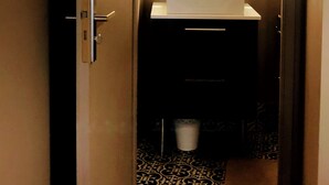 Ein schmaler Flur führt zu einem Badezimmer mit einem weißen Waschbecken, einem Spiegel mit beleuchtetem Rahmen und einem fußbodenmuster.