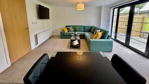 Een moderne woonkamer met een hoekbank, een eettafel en een aan de muur bevestigde televisie.