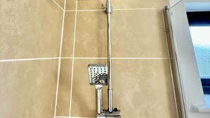 Een douche met regenstortdouche en handdouche, in een betegelde badkamer met uitzicht op het buitengebied.