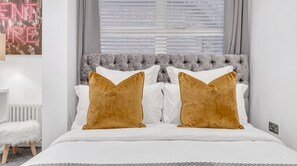 A bed with a tufted headboard, white bedding, and two brown pillows. - Modern London 1 Bedroom Apartment Camberwell, Oval & Elephant & Castle (LONDON)
