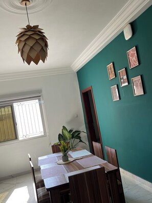 Un coin repas avec une table dressée pour quatre personnes, un luminaire suspendu, une plante en pot et des œuvres d’art encadrées accrochées au mur.