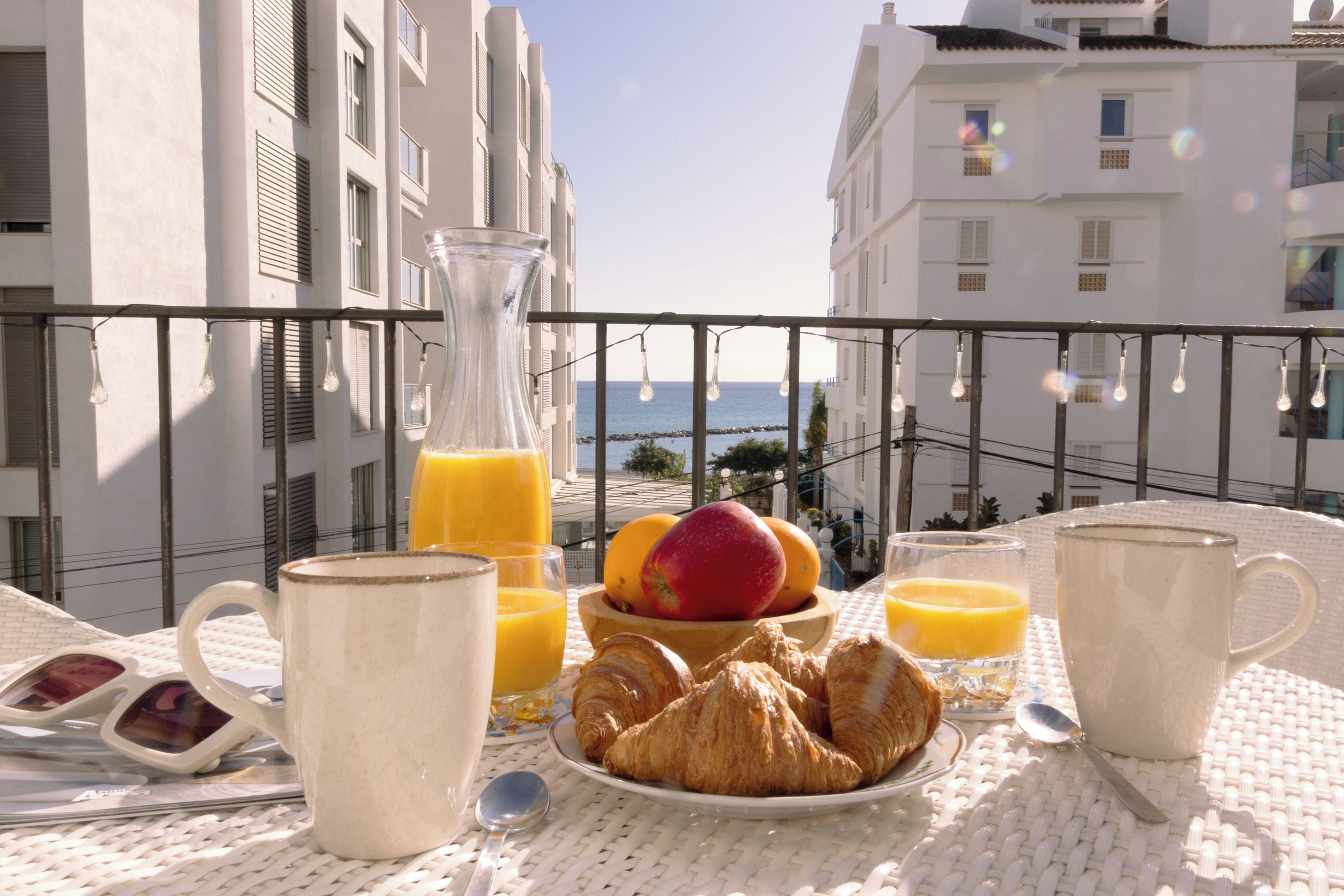 Un plateau de petit-déjeuner installé sur un balcon, avec des croissants, des fruits, du jus d’orange et du café.