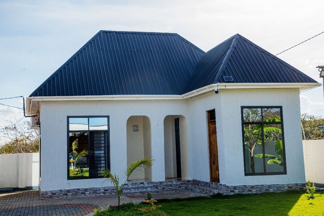 A single-story house with a dark roof, white exterior walls, and a small front porch.