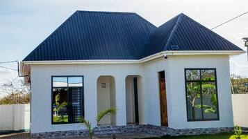 A single-story house with a dark roof, white exterior walls, and a small front porch.