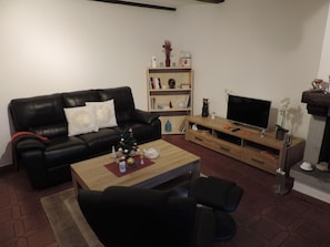 Ein Wohnzimmer mit einer schwarzen Ledersofa, einem Holztisch, einer TV-Kommode und einem Bücherregal.