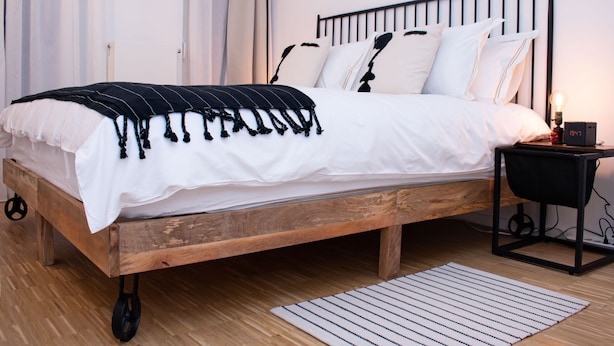 A wooden bed with white bedding, a globe wall decoration, and a bedside table with a lamp. - "Industrial Sanctum" by Interhome (Brussels)