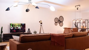 A modern living room with a brown sofa, a television, a tripod, and a ceiling light fixture. - "Industrial Sanctum" by Interhome (Brussels)